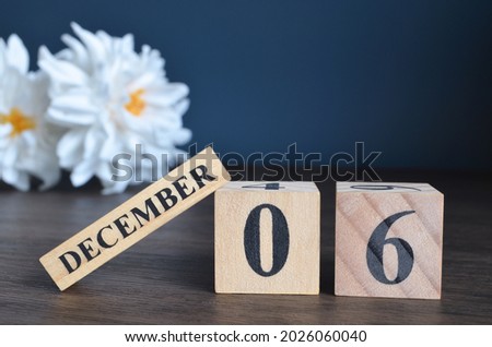 December 6, Date cover design with calendar cube and white Paeonia flower on wooden table and blue background.