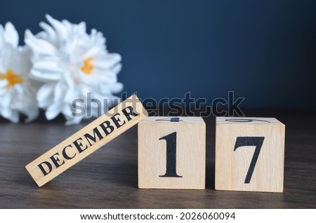 December 17, Date cover design with calendar cube and white Paeonia flower on wooden table and blue background.