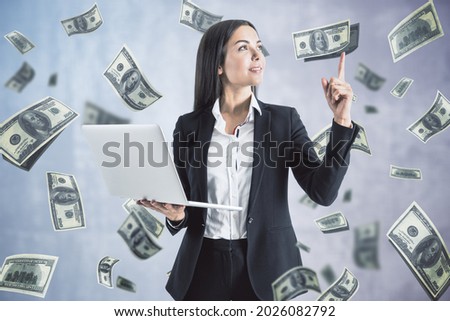 Attractive happy european businesswoman with laptop pointing up on white background with dollar banknote rain. Jackpot, wealth and lottery win concept