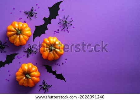 Happy Halloween holiday concept. Halloween decorations, pumpkins, bats, spiders on purple background. Halloween party greeting card mockup with copy space. Flat lay, top view, overhead.