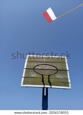 red and white flag made of textured paper and basketball hoop on a blue sky background