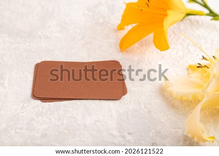 Brown paper business card mockup with orange day-lily flower on gray concrete background. Blank, side view, copy space, still life. spring concept.