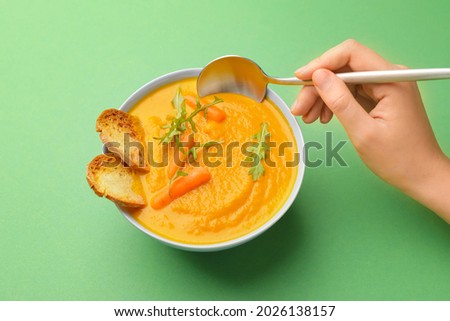Woman eating tasty carrot cream soup on color background