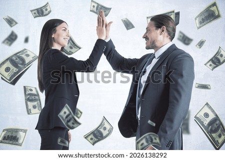 Attractive young european businesswoman and man hi-fiving each other on white background with dollar banknote rain. Jackpot, teamwork, wealth and lottery win concept