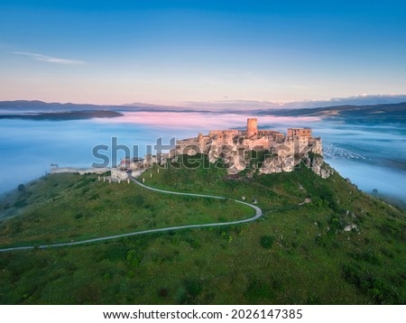 Aerial, early morning view of Spiš Castle, standing above mist, lit by morning sun, with windings road on the hill. Magic, colorful moment,  landscape photography. Slovakia. Listed in UNESCO.