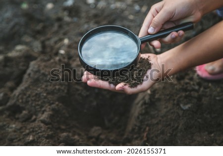 The child examines the ground with a magnifying glass. Selective focus. Nature.