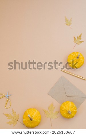 Autumn composition with small yellow pumpkins, fallen maple leaves, envelope, pen and scissors on a beige background with copy space.