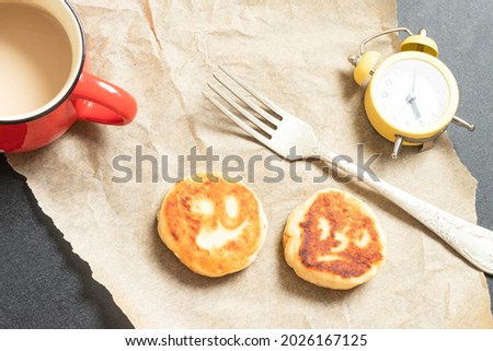 Breakfast on the table top view: a cup of coffee, two pancakes with sad drawn faces, beautiful fork, alarm clock on baking paper. Cheerful early morning, halloween, funny food, emoji concept. Nobody.
