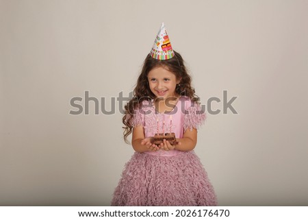 beautiful happy brown-haired girl with curly hair in a pink dress with a piece of cake in her hands birthday