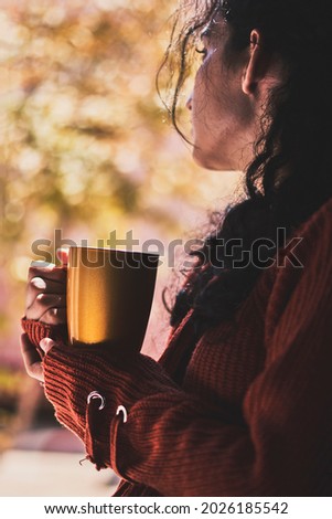 Cold autumn days - a young multi-racial female drinks coffee in a cozy windowsill. Middle-eastern or mixed-race woman enjoys weekend drinking hot tea near the windows Royalty-Free Stock Photo #2026185542