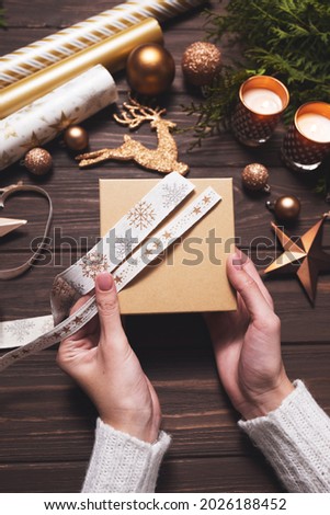 Women's hands pick up a festive ribbon for wrapping a Christmas gift. Diy hobby.