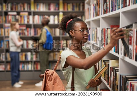 Waist up portrait of female Africa-American student choosing books in college library, copy space Royalty-Free Stock Photo #2026190900