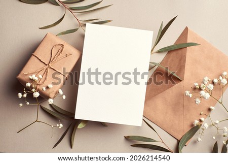 Greeting card mockup with gift box, envelope and eucalyptus and gypsophila twigs on beige background. Card mockup with copy space. Royalty-Free Stock Photo #2026214540