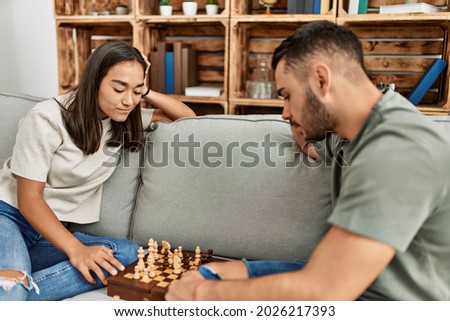 Young latin couple smiling happy playing chess at home.
