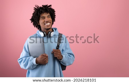 Positive African American teen student with backpack, tablet pc and headphones studying online on pink studio background, banner with free space. Happy black adolescent having remote college education Royalty-Free Stock Photo #2026218101
