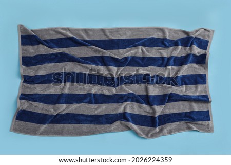 Crumpled striped beach towel on light blue background, top view