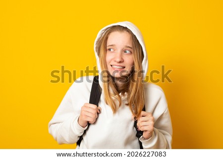 Funny young girl dressed white hoodie on yellow  background with backpack. Portrait of cool schoolgirl with backpack.