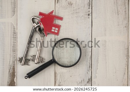 The concept of sale, mortgage and rent of housing and real estate. Home sale. Keychain in the shape of a house with magnifying glass on a white wood background . Copy space