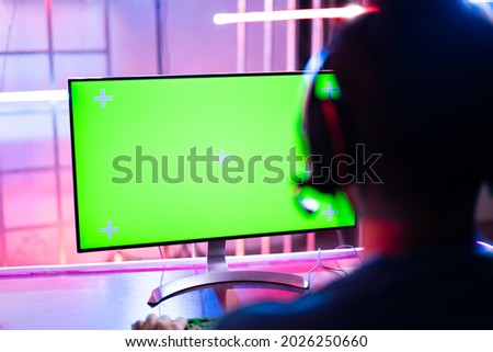 Shoulder shot of professional video gamer playing video game on Agreen screen computer monitor - concept of esports tournment on neon light background.