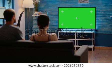 Green screen on television at home in living room used by young man and woman for copy space design of chroma key and modern equipment. People with isolated template for mockup background