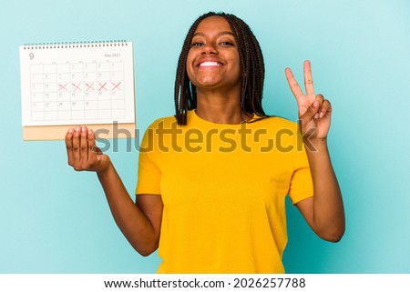 Young african american woman holding a calendar isolated on blue background  showing number two with fingers. Royalty-Free Stock Photo #2026257788