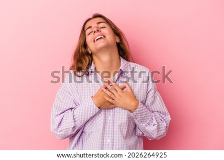 Young caucasian woman isolated on pink background  has friendly expression, pressing palm to chest. Love concept.