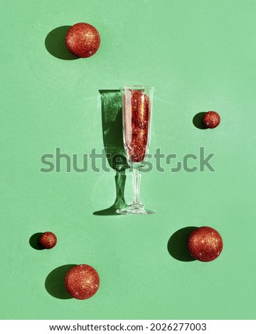 Champagne glass with bright red glitters, Christmas holiday balls, sparkling festive drink with dark shadows. New year celebration concept.