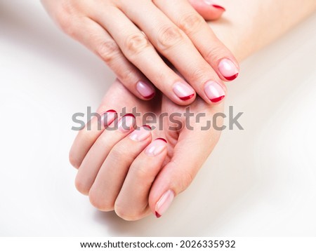 Female hands with a trendy autumn french manicure with red tips at the free edge of the nail. White background and fall leaves decor Royalty-Free Stock Photo #2026335932
