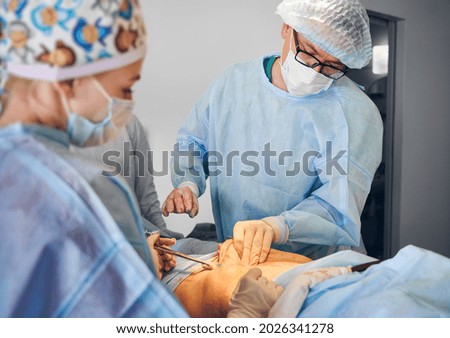 Plastic surgeon and assistant performing plastical surgical operation in hospital, removing excess fat from patient abdomen in operating room. Concept of medicine, abdominoplasty and aesthetic surgery