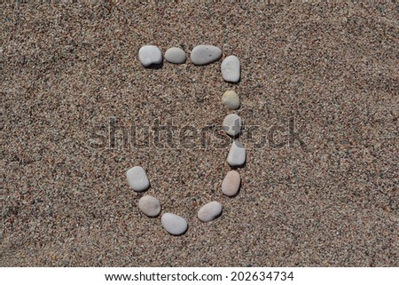 J letter made of stones on sand 