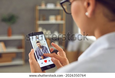 Woman looking for romantic relationship. Single lady holding smartphone and giving like to photo of young man on online dating mobile app or website. Closeup display shot, close up view over shoulder