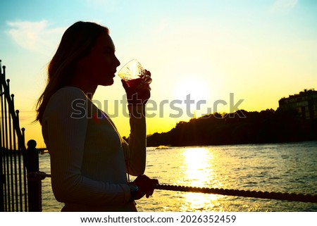 Silhouette photo of a woman drinking orange juice  from a glass at sunset .