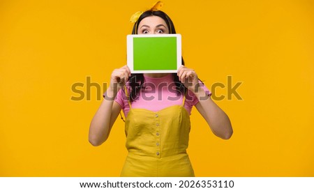 Amazed woman covering face with digital tablet isolated on yellow