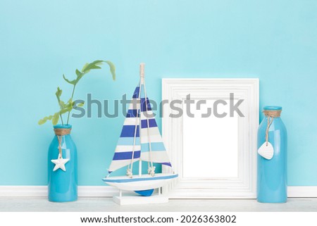 Background mockup template with shabby chic, rustic vertical picture frame, wooden sail boat, decorated vases, one with fern leaves in front of blue wall, inner frame isolated with clipping path