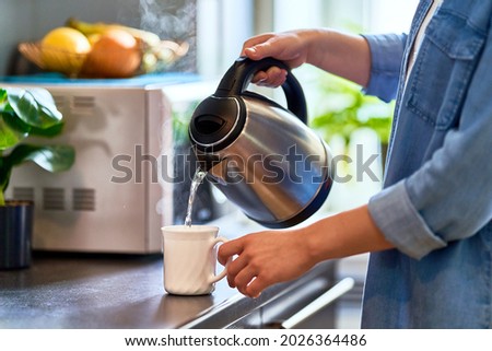 Female hands pouring boiling water from a modern metal stainless kettle in a glass cup for brewing tea in the kitchen at home Royalty-Free Stock Photo #2026364486
