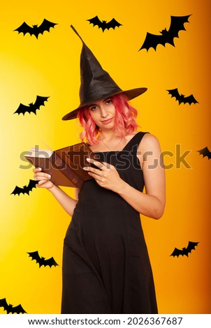 Evil female wizard holding a magic broom. Indoor photo of a wicked woman in a witch costume posing in halloween with a book of spells in her hands.