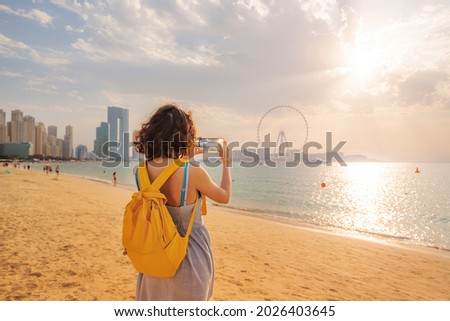 Woman travel blogger takes pictures for social networks of skyscrapers on Bluewaters island and the famous Ain Ferris Wheel in Dubai