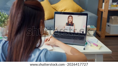 Young Asia girl with casual use computer laptop video call learn online with teacher write lecture notebook living room at house. Isolate education online e-learning coronavirus pandemic concept.