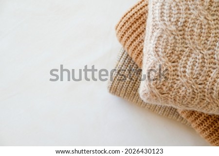 Bunch of knitted warm pastel color sweaters with different knitting patterns folded in stack, clearly visible texture. Stylish fall-winter season knitwear clothing. Close up, copy space for text. Royalty-Free Stock Photo #2026430123