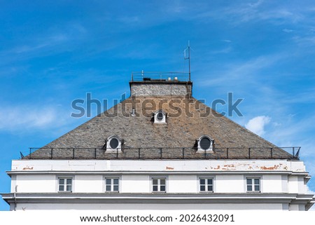 The large roof is covered with the flat tile of an old house with three round windows in the attic.