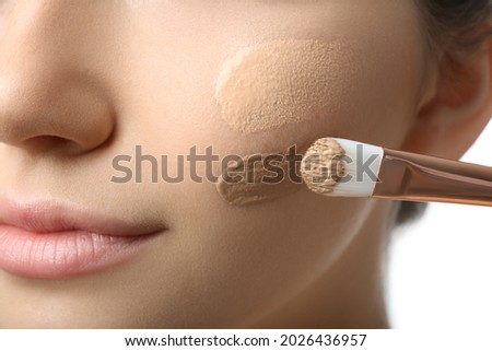 Girl applying foundation and concealer with brush on white background, closeup. Face contouring Royalty-Free Stock Photo #2026436957