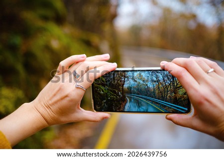 A female hand holding an mobile Phone trying to capture the awesome colors of autumn in the forest. Fall Getaway