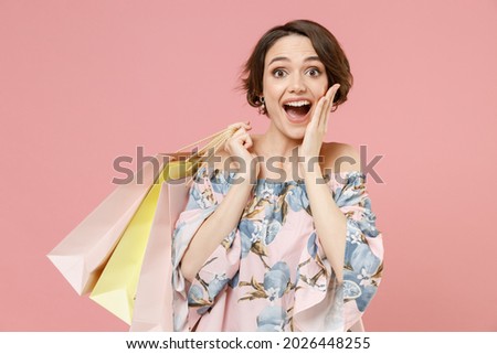 Young excited fun amazed impressed happy woman with short hairdo wear trendy stylish blouse keeping package bags with purchases after shopping hold face isolated on pastel pink color background studio