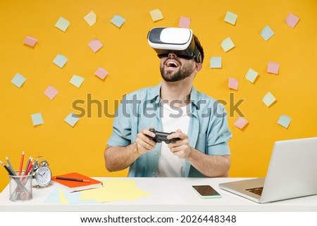 Young fun gambling employee business man in shirt sit work at white office desk with pc laptop play pc game with joystick console watching in vr headset pc gadget isolated on yellow background studio Royalty-Free Stock Photo #2026448348