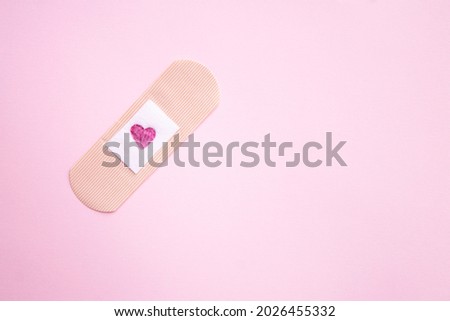 Love concept. Medical plaster with a picture of a heart on a pink background. Background of the day of lovers or unrequited love. Greeting card top view.