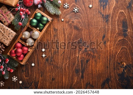 Christmas fir tree branches decor red and green Christmas balls, wooden snowflakes and stars on wood background for your xmas greetings. Top view with copy space. Christmas greeting card.