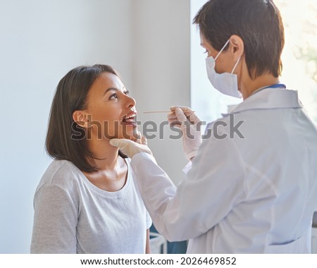 Pharyngitis and laryngitis treatment. Middle-aged woman general practitioner in face protective mask examining throat and mouth of young afro american female patient visiting ENT doctor in clinic Royalty-Free Stock Photo #2026469852