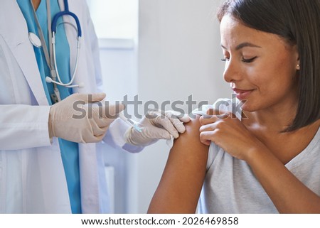 Young afro american woman receiving injection of coronavirus vaccine during appointment in clinic, doctor in uniform with syringe vaccinating female patient in hospital. Immunisation and vaccination Royalty-Free Stock Photo #2026469858
