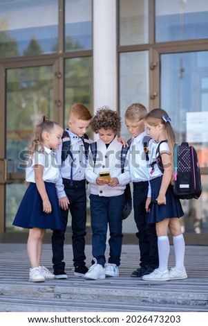 A group of little schoolchildren stands at the school and looks at the phone Royalty-Free Stock Photo #2026473203