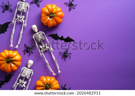 Happy Halloween holiday concept. Flat lay composition with scary skeletons, pumpkins, spiders, bat silhouettes on purple background. Top view, overhead.